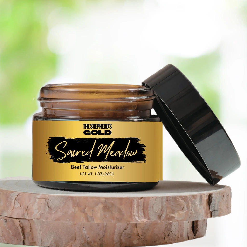 Jar of 'The Shepherd's Gold Sacred Meadow' beef tallow moisturizer on a wooden surface with a blurred green background.